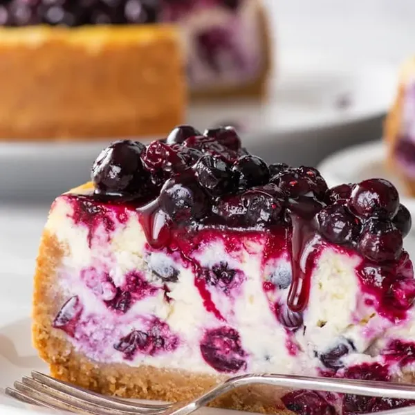 Overhead view of the whole cheesecake topped with blueberry compote, one slice lifted onto a plate