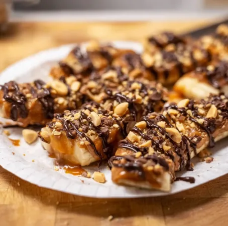 Healthy banana treats drizzled with chocolate and caramel sauce arranged on wooden cutting board