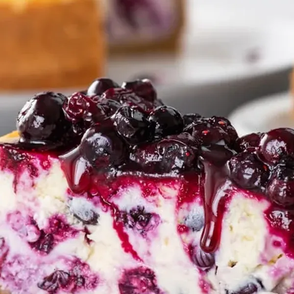 Close-up of burst blueberries streaking purple through the dense cheesecake filling above a golden graham crust
