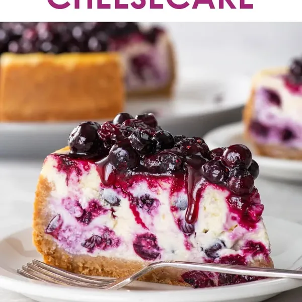 A tall slice of blueberry cheesecake with glossy compote spilling down the creamy marbled side